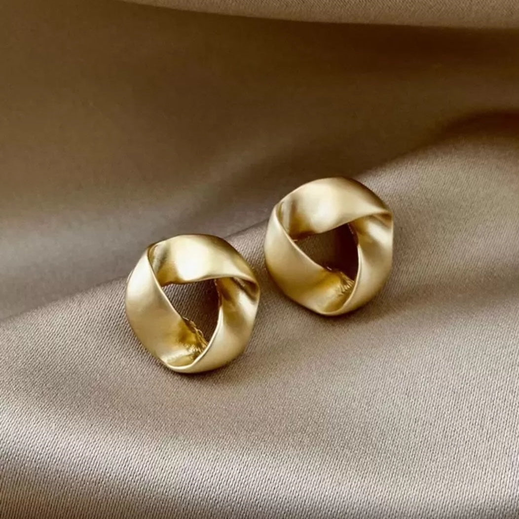 Pair of satin gold knot earrings on a beige fabric background