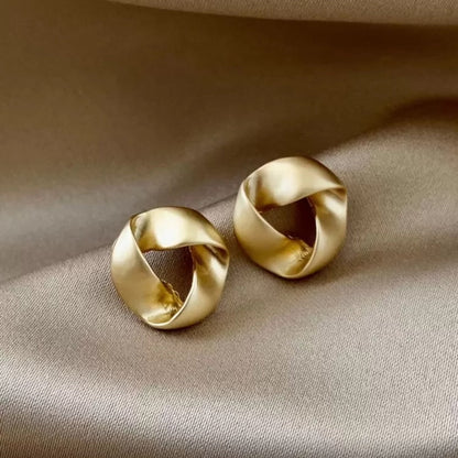 Pair of satin gold knot earrings on a beige fabric background