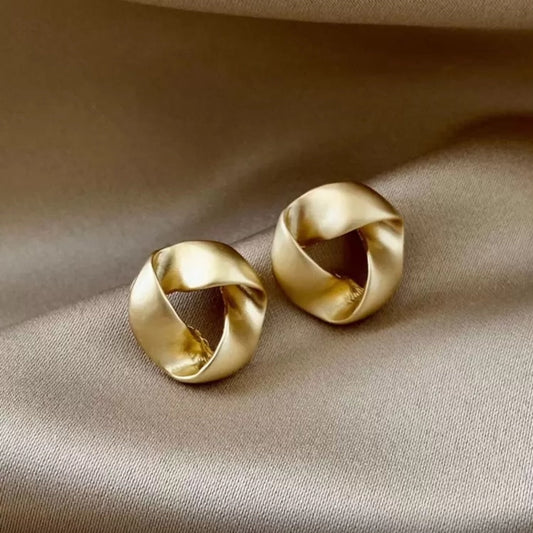 Pair of satin gold knot earrings on a beige fabric background