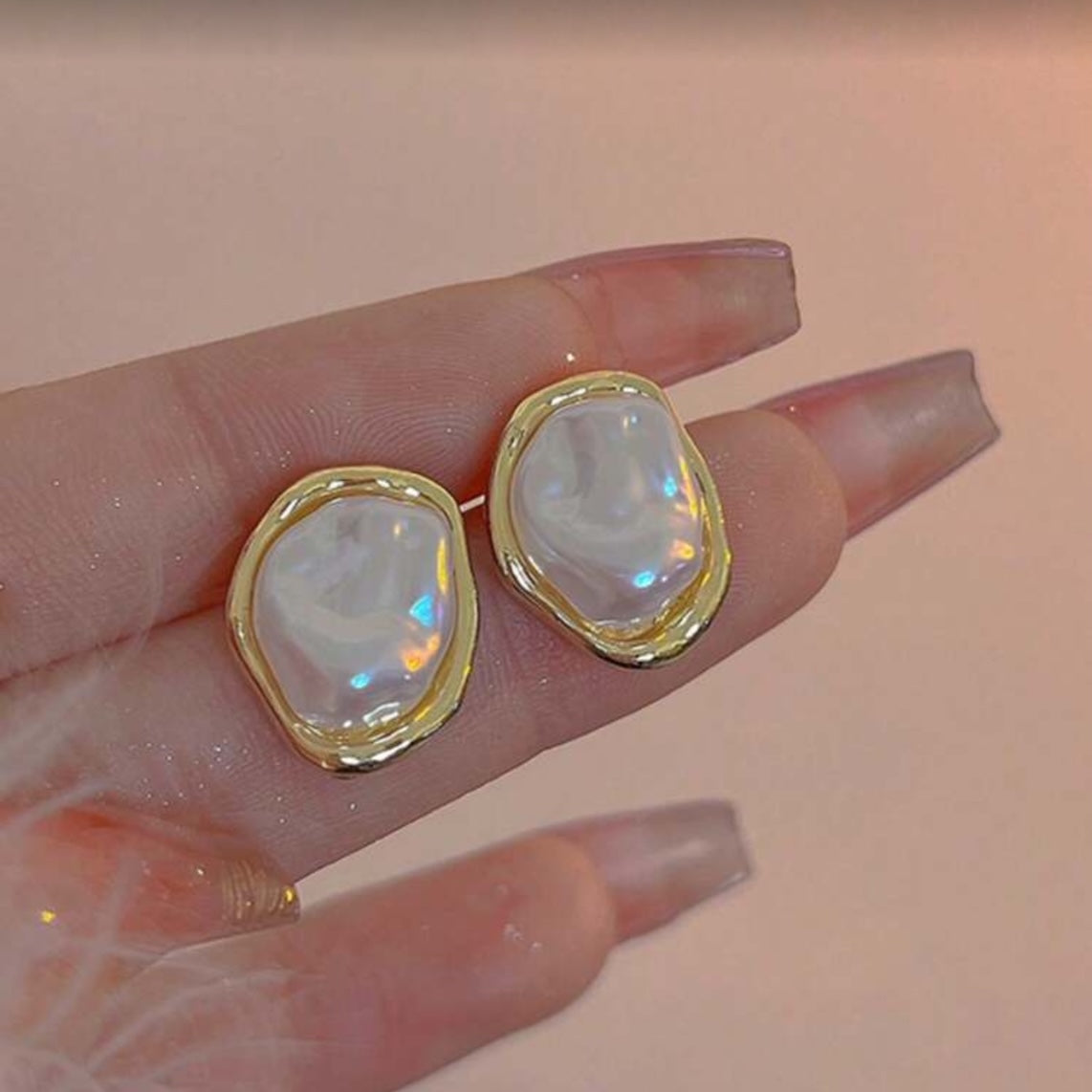 Iridescent Glow Pearl Studs held between fingers against a neutral background