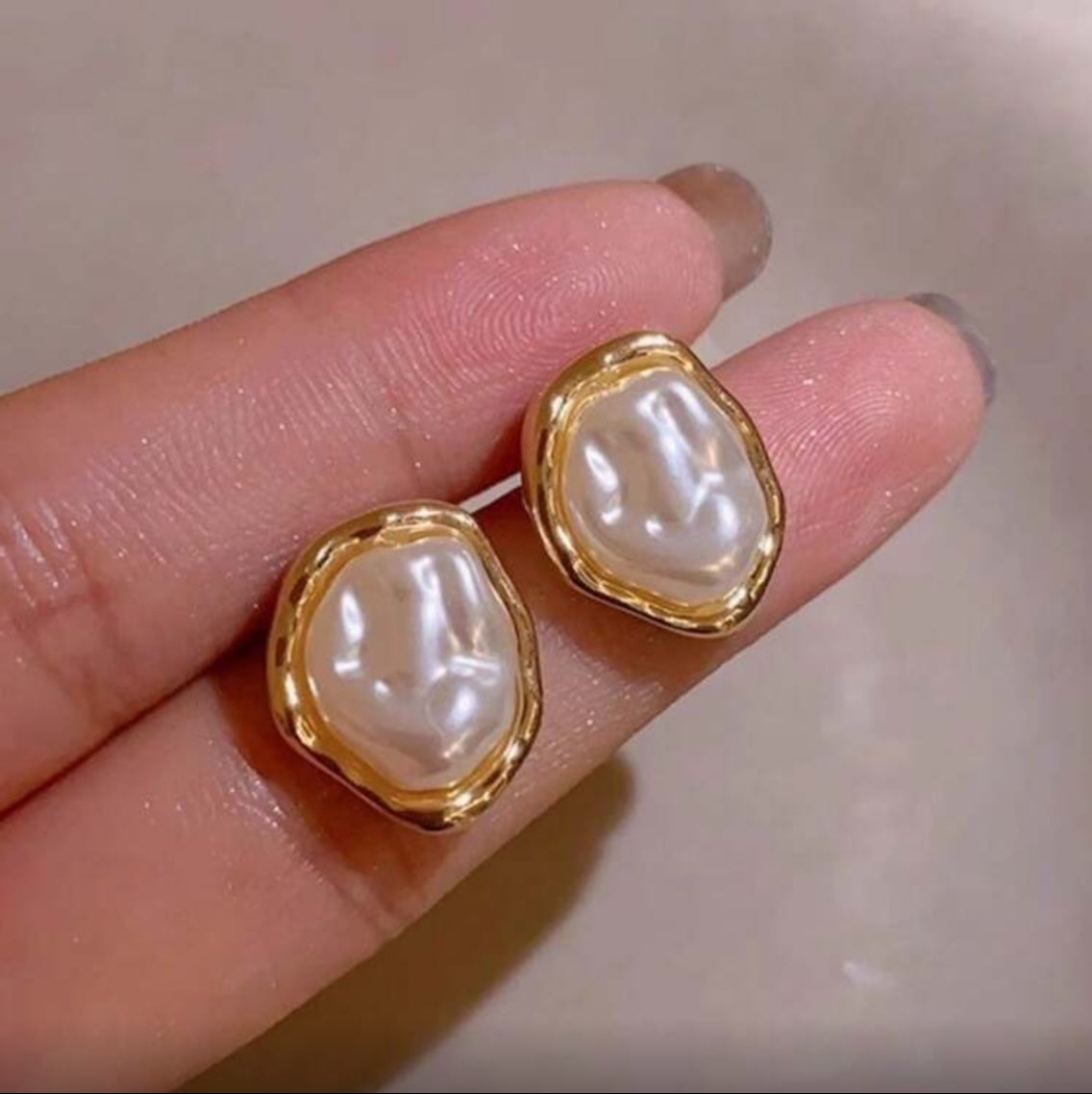 Iridescent Glow Pearl Studs held between fingers against a neutral background