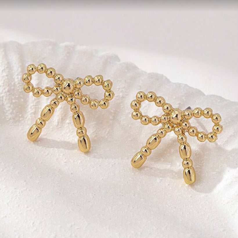 Gold Beaded Bow Earrings on a white textured surface