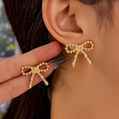 Gold Beaded Bow Earrings being worn and held up to an ear.