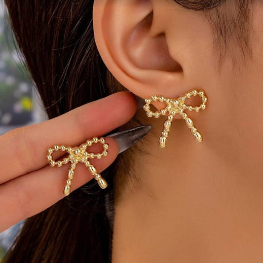 Gold Beaded Bow Earrings being worn and held up to an ear.