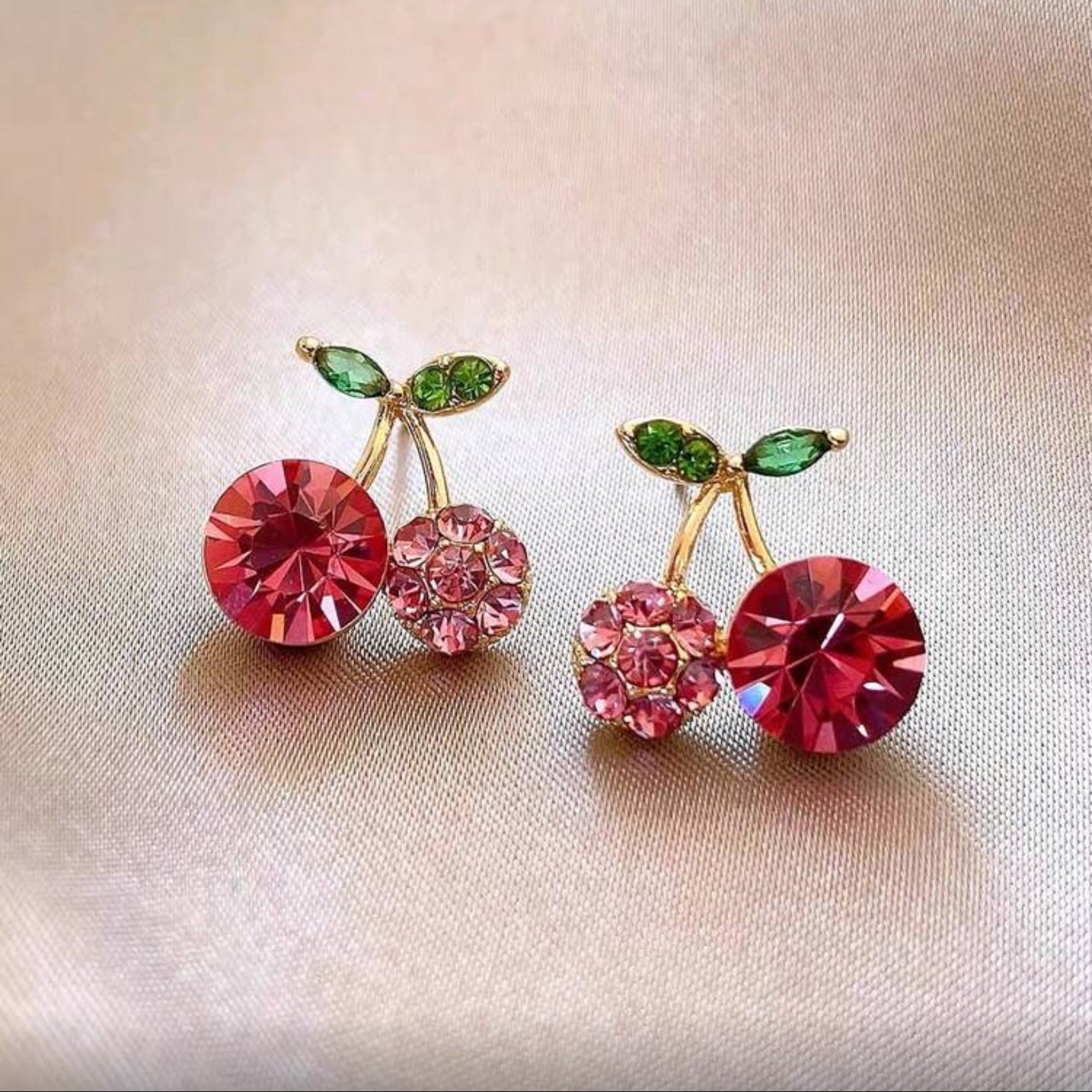Pink Zircon Cherry earrings with red, pink, and green gemstones on a light background