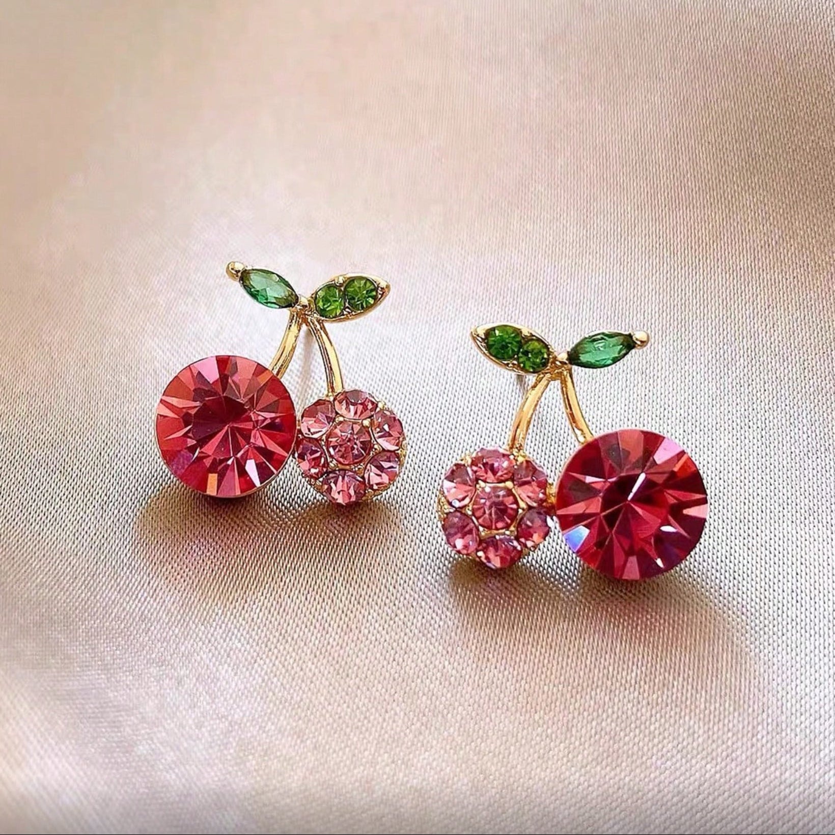 Pink Zircon Cherry earrings with red and green gemstones on a beige background