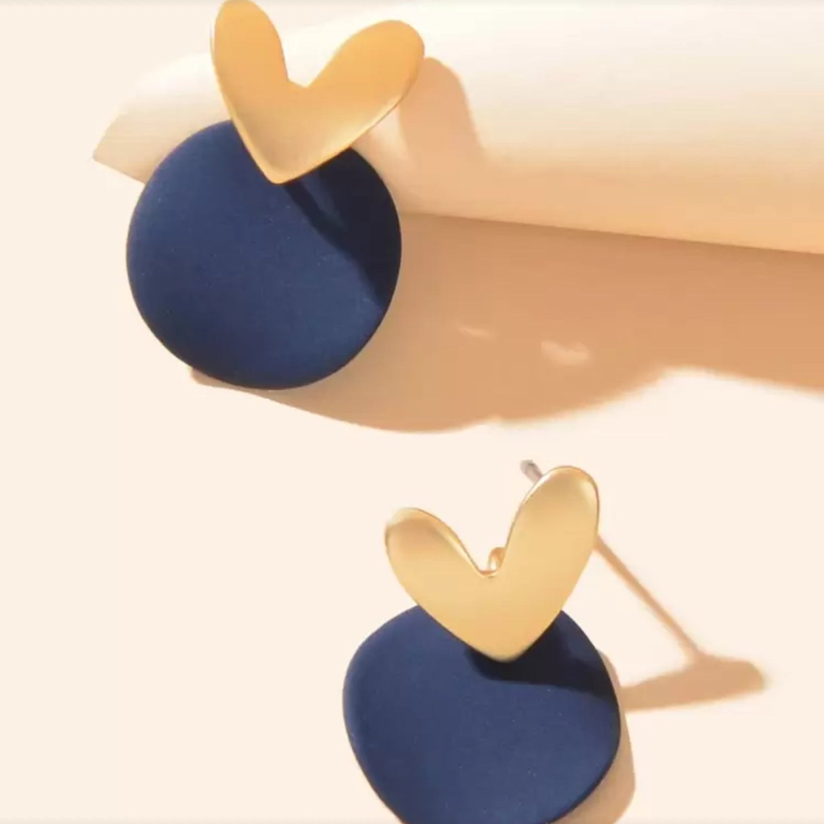 Midnight Blue & Gold Heart Earrings with gold heart-shaped tops and blue circular bases on a beige background