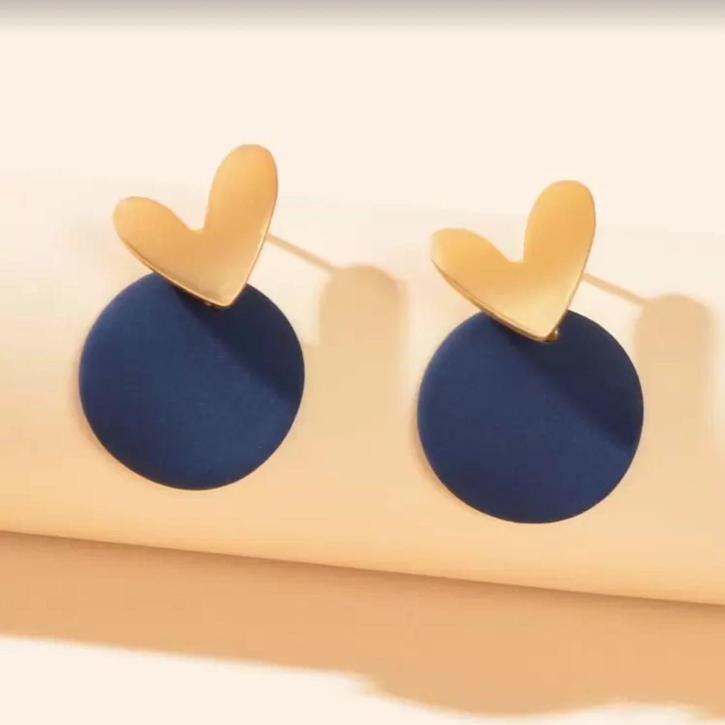 Midnight Blue & Gold Heart Earrings on a beige stand.