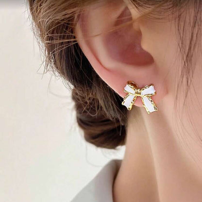 White and Gold Bow Earrings worn by a person with a neutral background