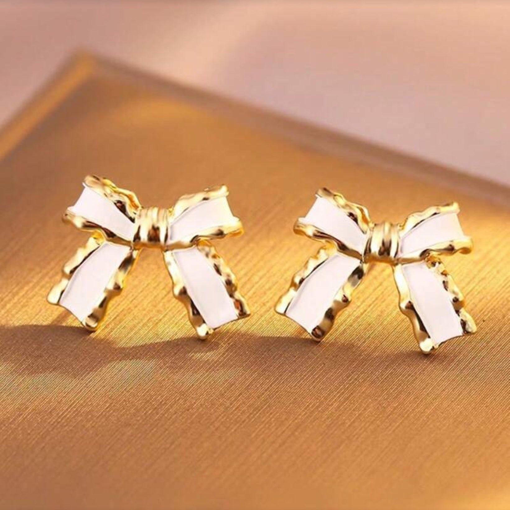 White and Gold Bow Earrings details on a gold surface