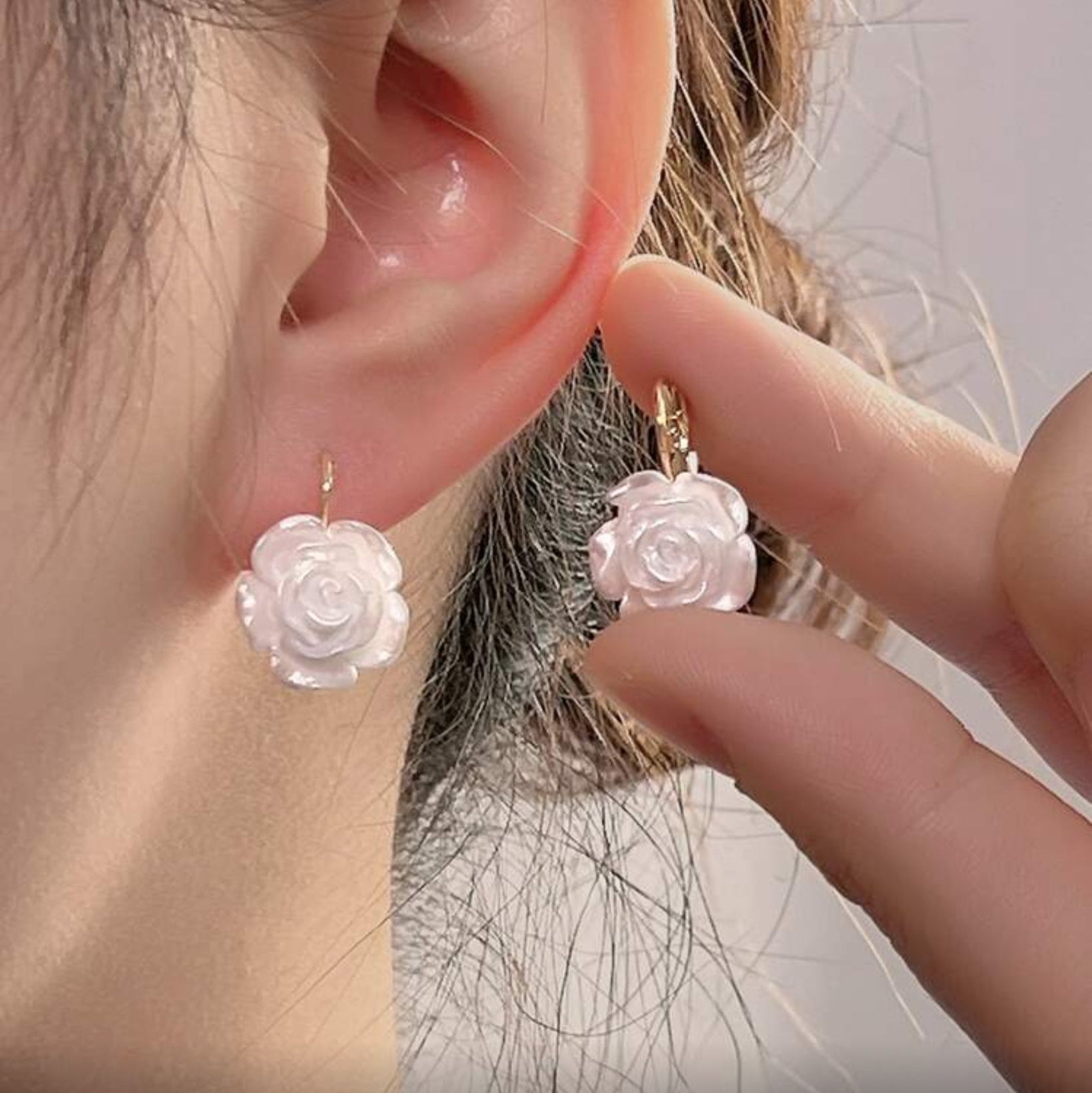 Close-up of a person wearing a White Rose Earring with a hand holding another similar earring.