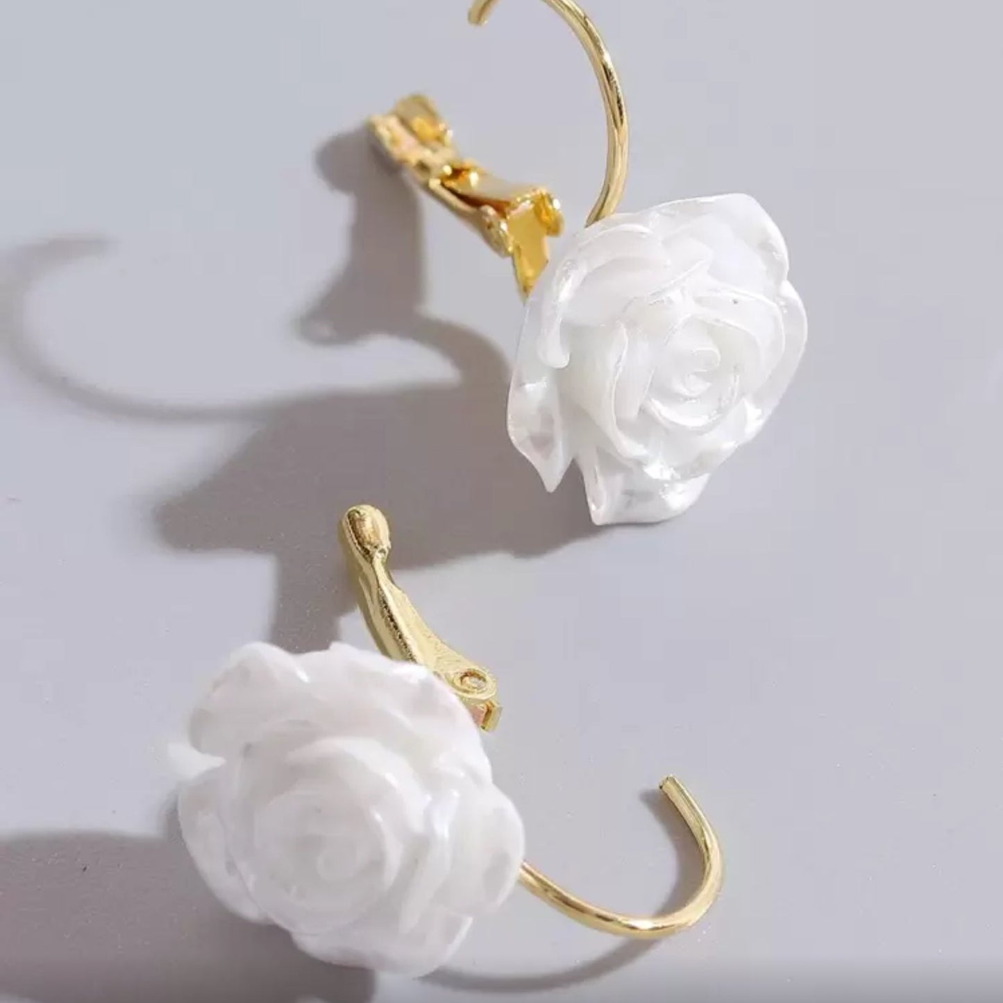 White rose earrings with gold hooks on a light gray background