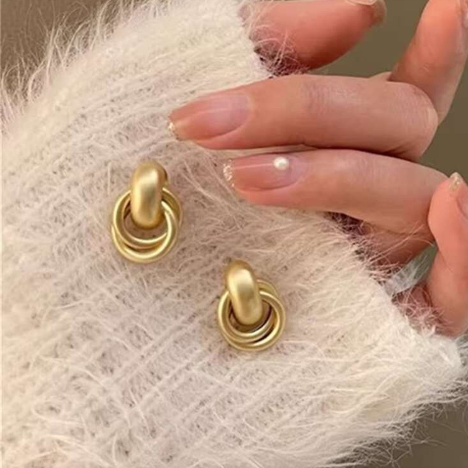 Satin Gold Hoop Earrings being worn on a textured white surface with a hand holding them.
