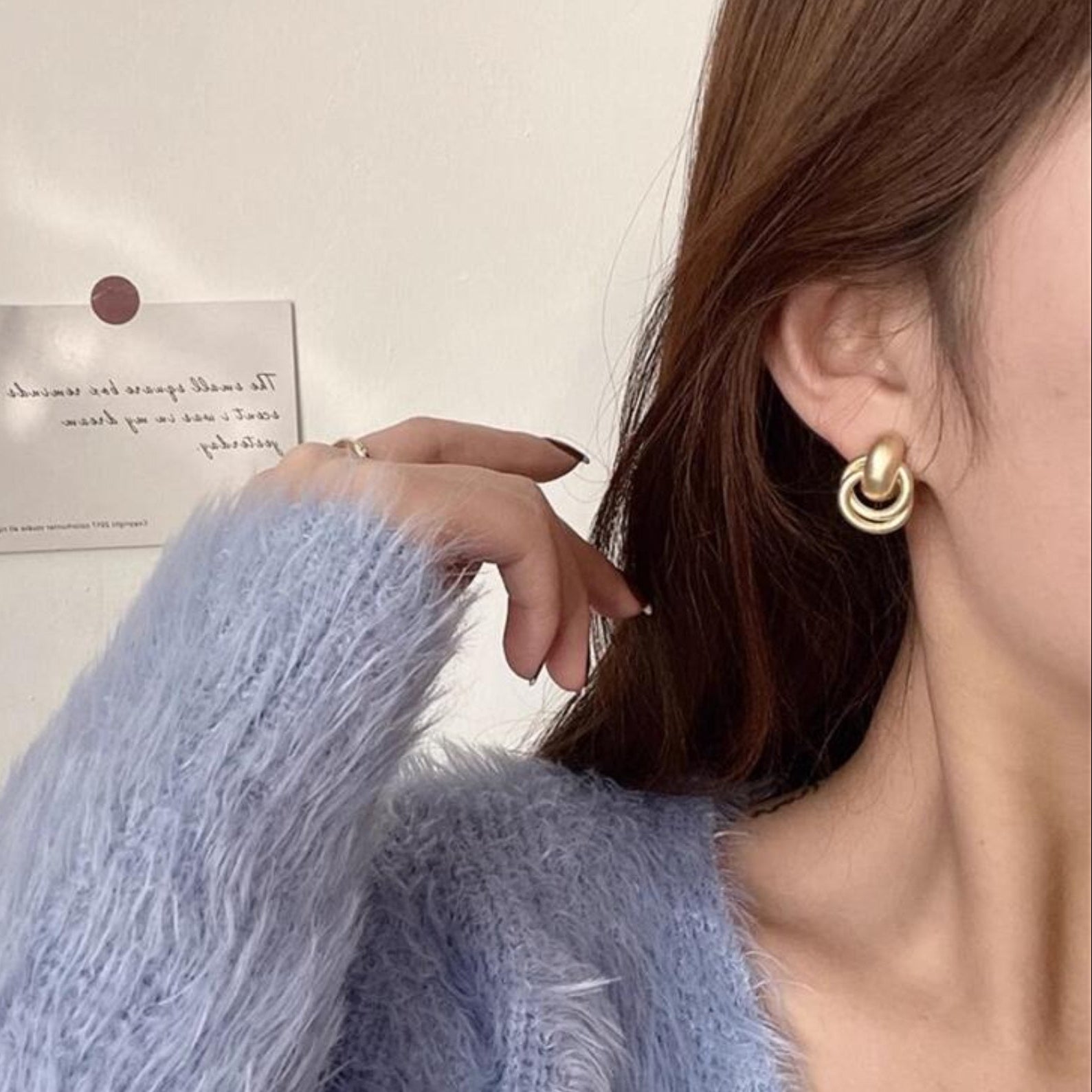 Close-up of a person wearing Satin Gold Hoop Earrings with a light blue textured sweater and blurred background.