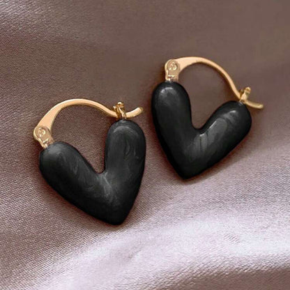 Black heart-shaped earrings with gold accents on a textured surface