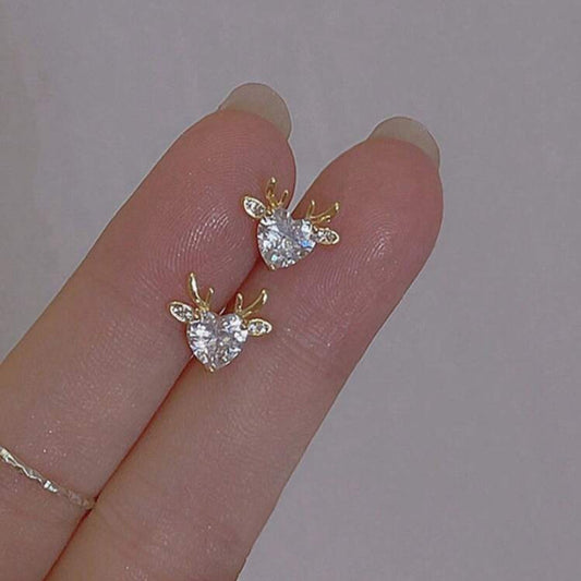 Gold Reindeer Zircon Heart Earrings held between fingers against a neutral background