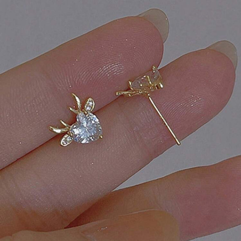 Gold Reindeer Zircon Heart Earrings held between fingers on a neutral background