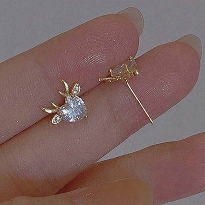 Gold Reindeer Zircon Heart Earrings held between fingers on a neutral background