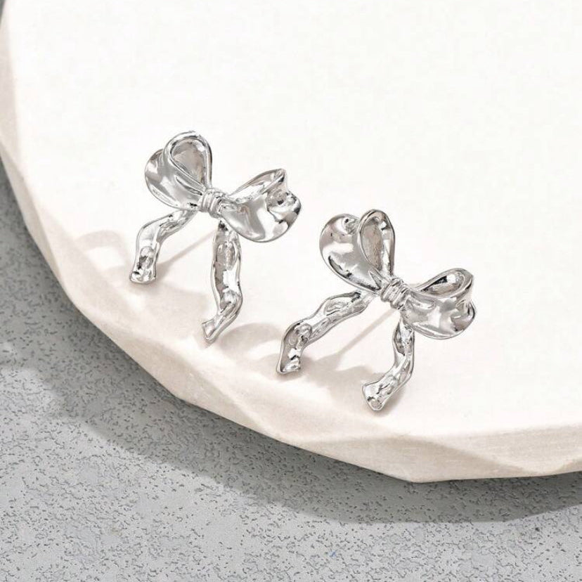 Silver Bow Ribbon Earrings on a white stone surface