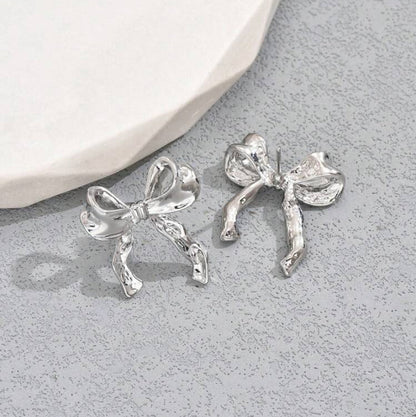 Silver Bow Ribbon Earrings on a gray surface
