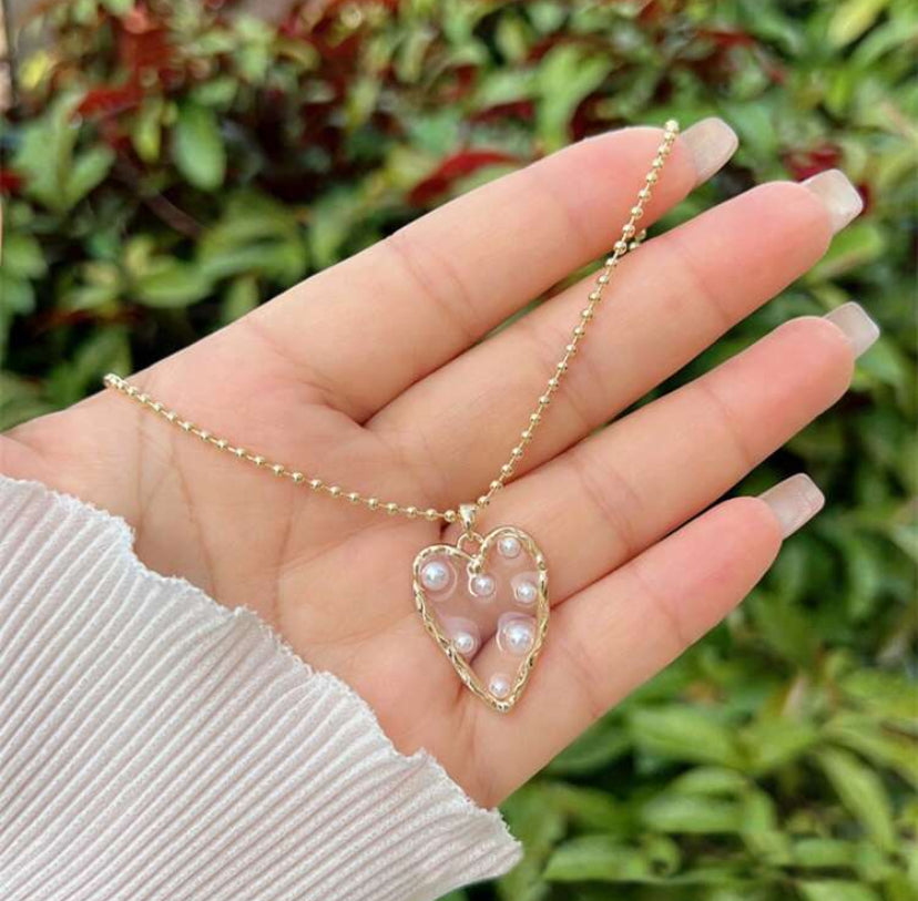 Hand holding a Golden Heart Pearl Necklace against a green leafy background.