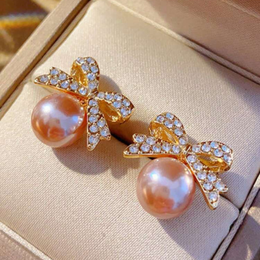 Peach Ornament Bow Earrings with gold bow designs on a beige jewelry box