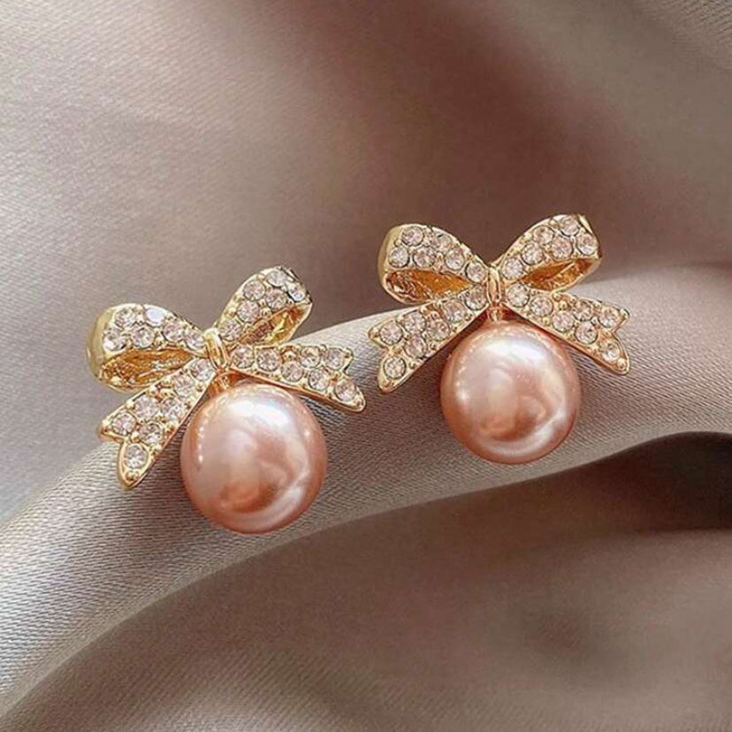 Pearl earrings with gold bow designs on a soft fabric background