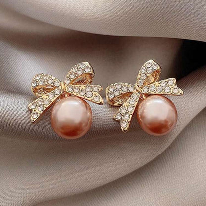 Peach Ornament Bow Earrings with pink pearls and gold bows on a beige fabric background