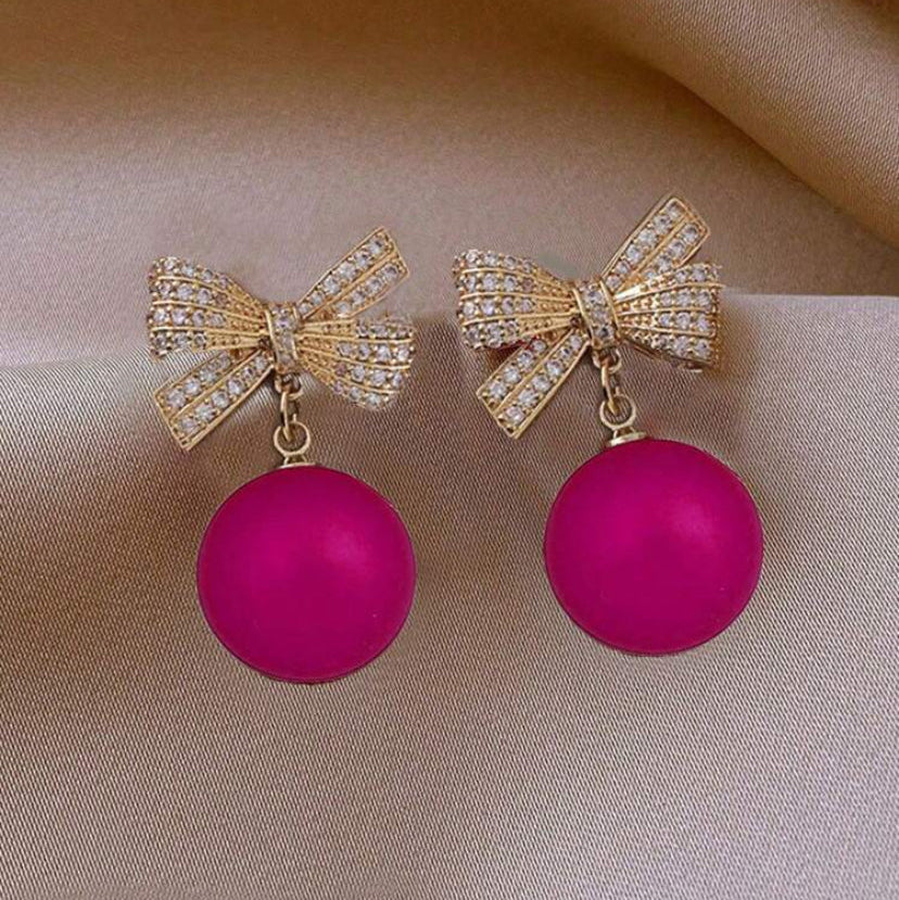 Pink ornament bow earrings with pink spherical charms on a beige background