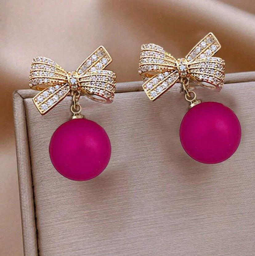 Pink Ornament bow earrings with pink spherical charms on a beige surface