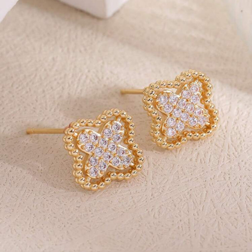 Gold Rhinestone Clover Earrings with clear gemstones on a beige surface