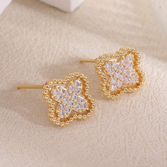Gold Rhinestone Clover Earrings with clear gemstones on a beige surface