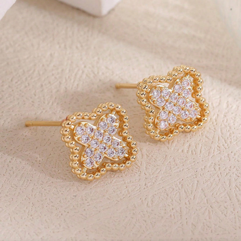 Gold Rhinestone Clover Earrings with clear gemstones on a beige surface