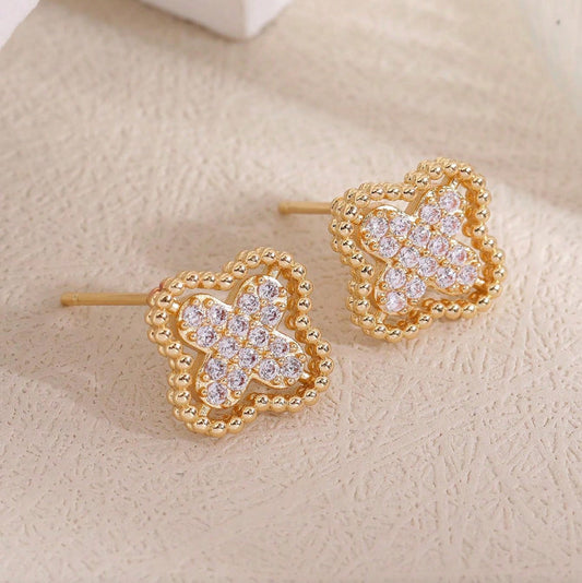 Gold Rhinestone Clover Earrings with clear gemstones on a beige surface