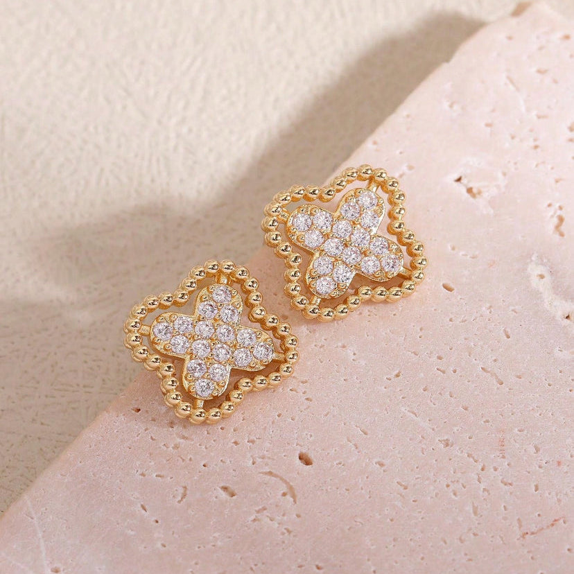 Gold Rhinestone Clover Earrings with diamond accents on a light pink stone background