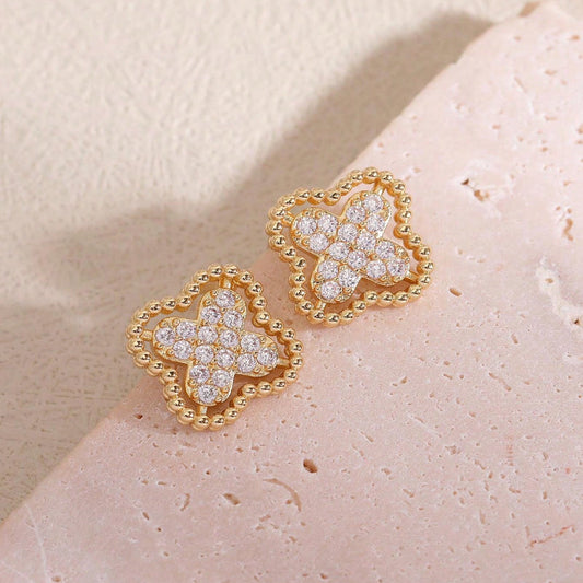Gold Rhinestone Clover Earrings with diamond accents on a light pink stone background