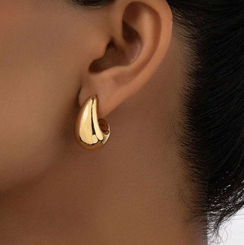 Gold Teardrop Hoop Earrings worn on an ear with a neutral background