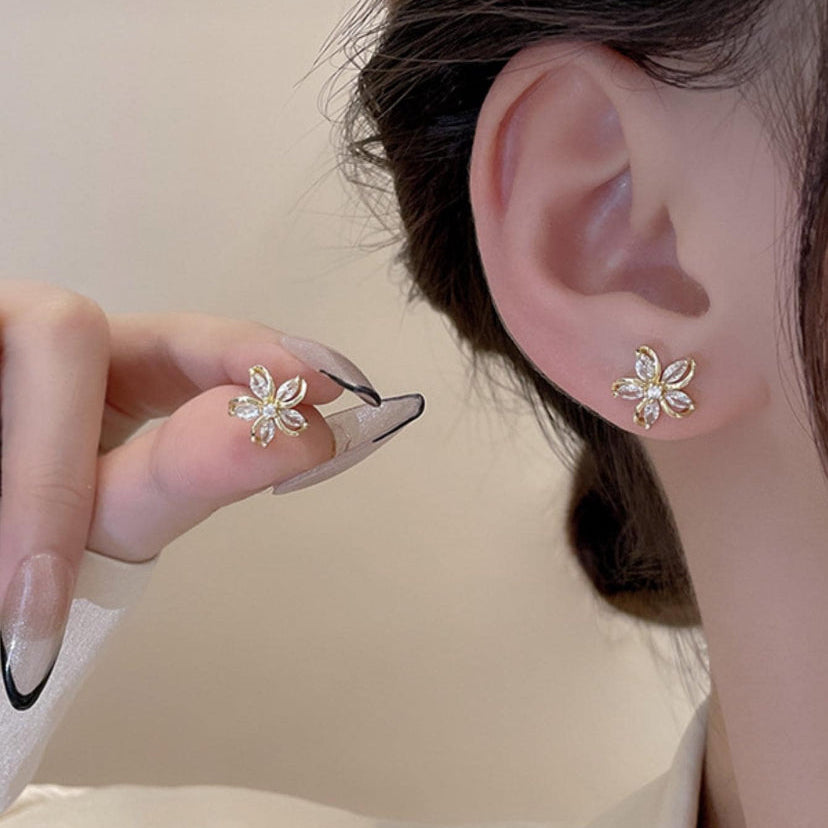 Close-up of an ear wearing a Gold Crystal Flower Earring with a hand holding another similar earring.