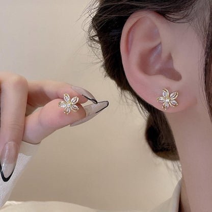 Close-up of an ear wearing a Gold Crystal Flower Earring with a hand holding another similar earring.