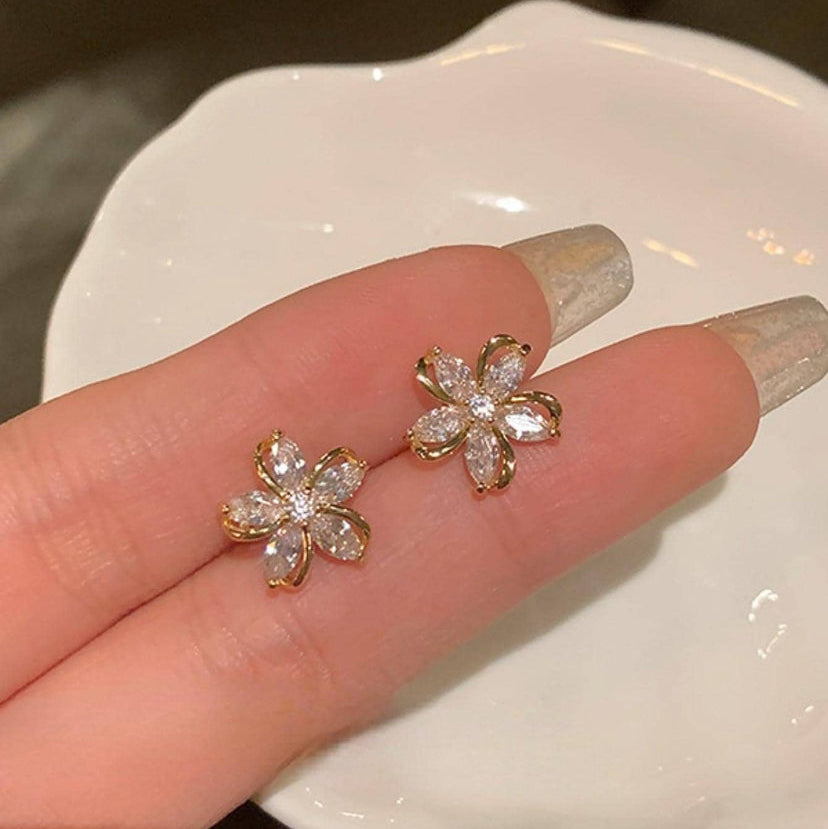 Gold Crystal Flower Earrings held between fingers on a white plate.