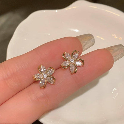 Gold Crystal Flower Earrings held between fingers on a white plate.