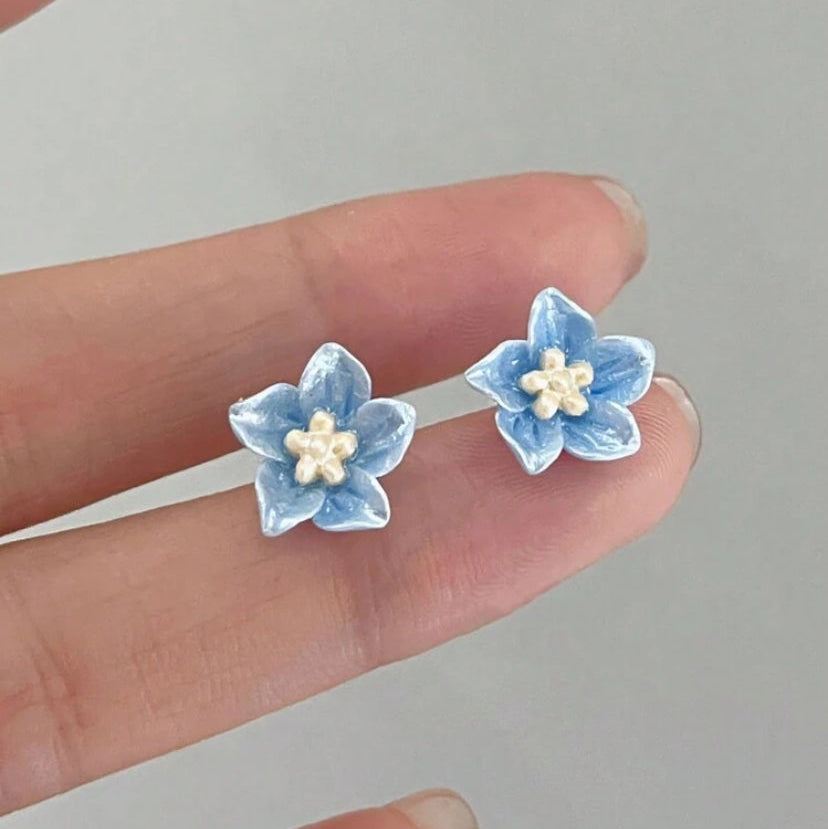 Blue petal blossom earrings held between fingers against a neutral background