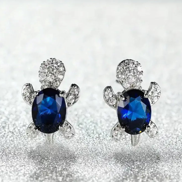 Blue Crystal Turtle Earrings with blue gemstones on a glittery surface