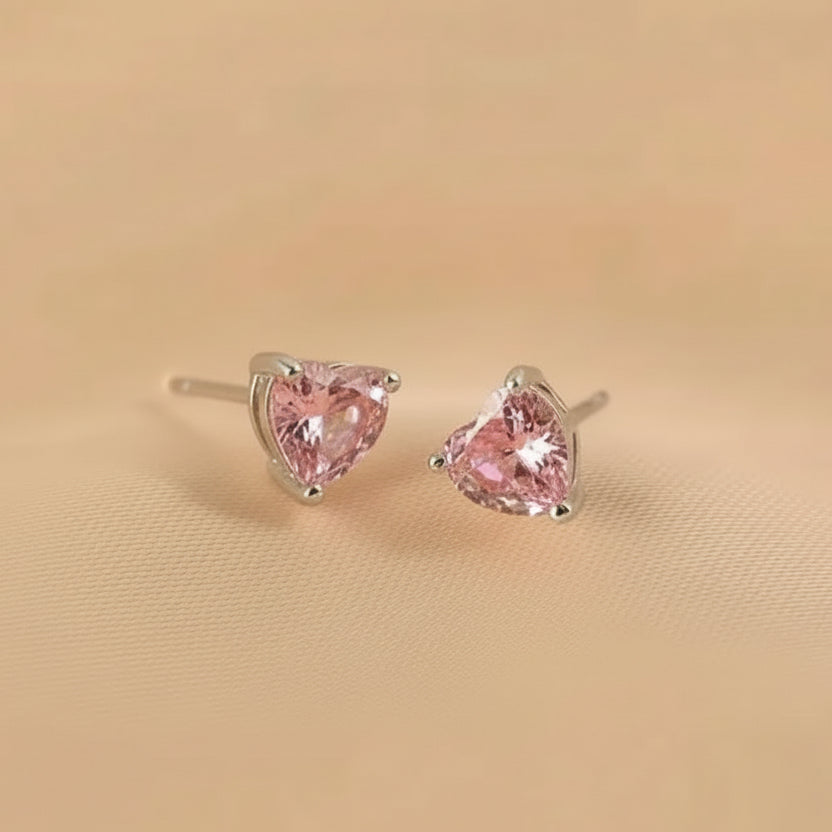 Pair of pink heart-shaped stud earrings on a beige background