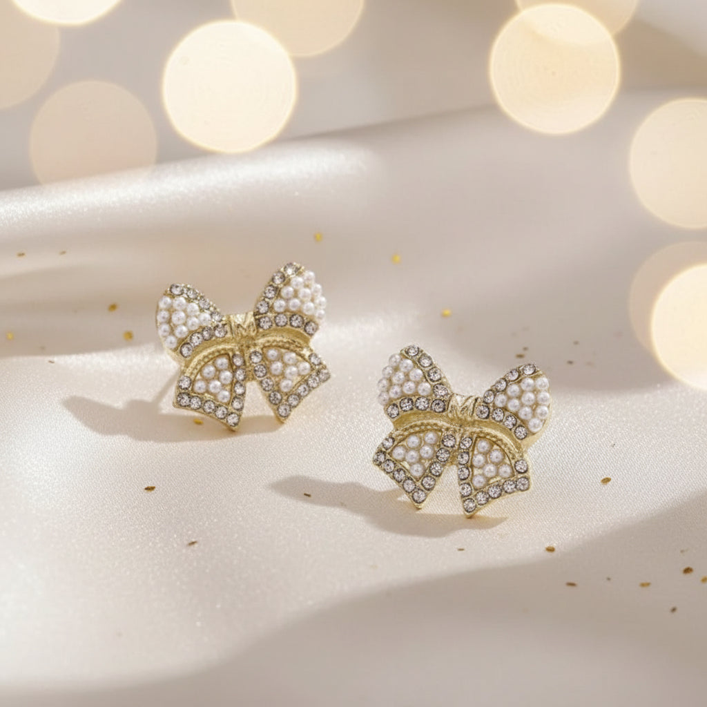 Classic Pearl Bow & CZ Earrings with pearl details on a soft surface with blurred lights in the background
