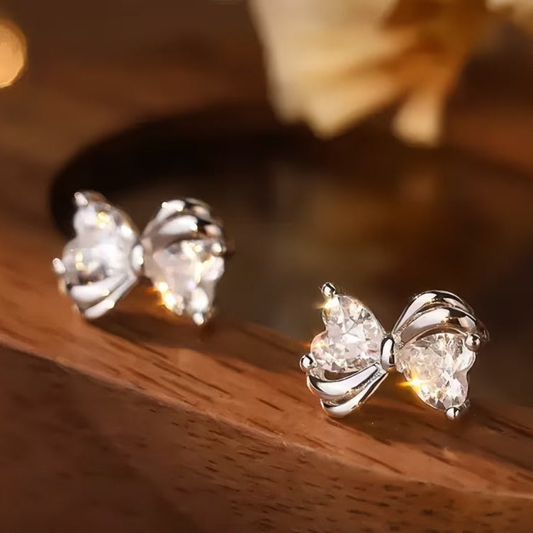 Mini Silver Heart Crystal Bow Earrings on a wooden surface with a blurred background