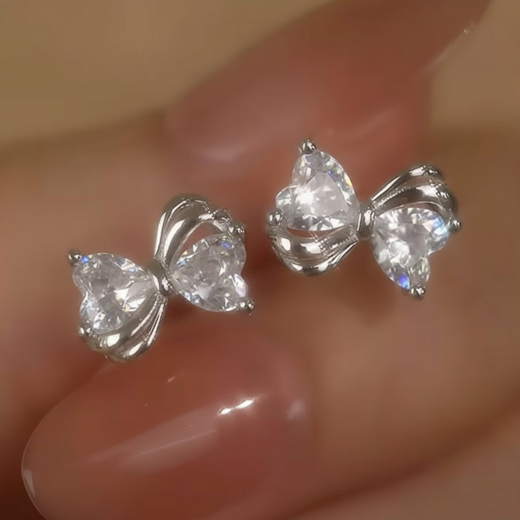 Mini Silver Heart Crystal Bow Earrings on a hand with a neutral background