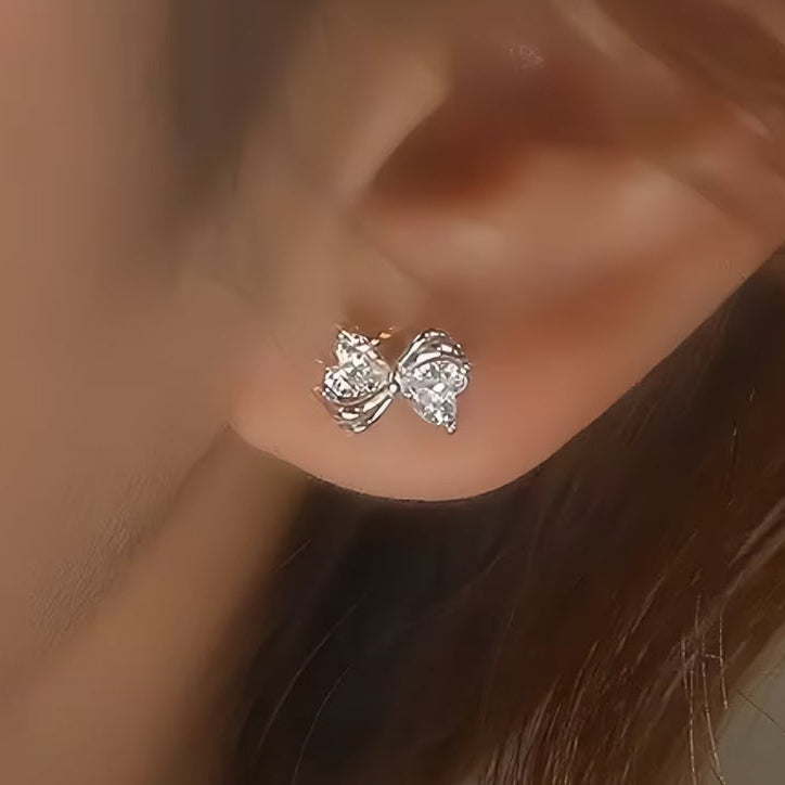 Mini Silver Heart Crystal Bow Earrings worn on an ear with a neutral background