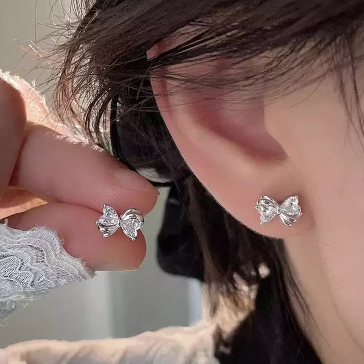Close-up of a person wearing Mini Silver Heart Crystal Bow Earrings.