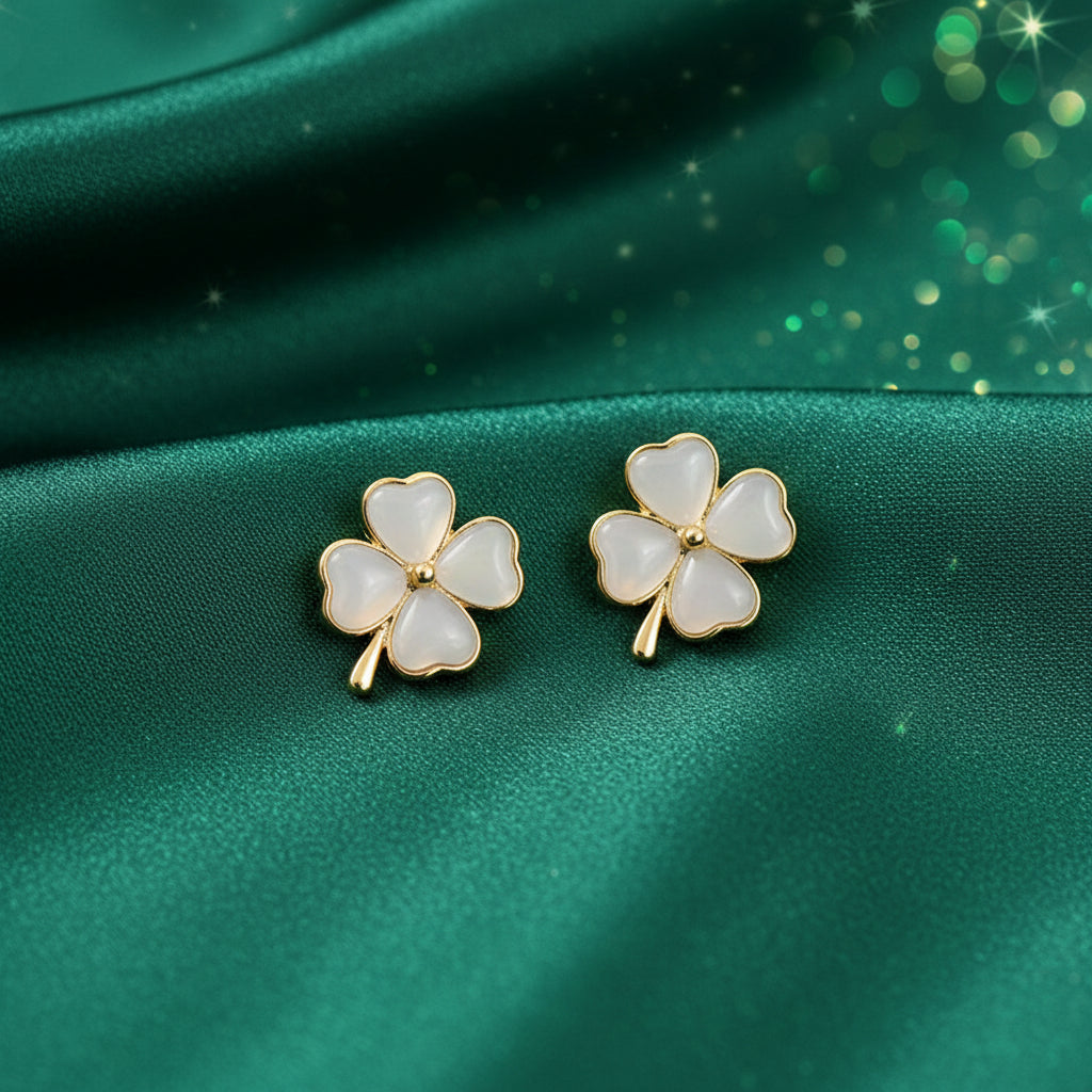 Pair of white Opalescent Clover Earrings with gold accents on a green fabric surface.